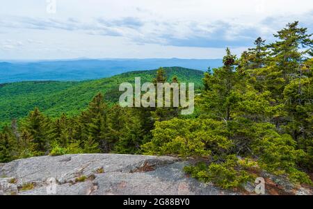 Südblick vom Gipfel des Mount Kearsarge. Felsiger Granitausschnitt und gestaute Fichtenbäume. Entfernte Gipfel und Grate. Rollins State Park, New Hampshire Stockfoto