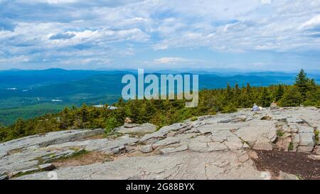 Nordblick vom Mt. Kearsarge Gipfel in Richtung Ragged Mountain. Wanderer, die sich auf dem Felsvorsprung entspannen. Gestaute Fichtenbäume. Entfernte Gipfel und Grate. Stockfoto