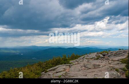 Nordblick vom Mt. Kearsarge Gipfel in Richtung Ragged Mountain. Granitausläufer und gestaute Fichtenbäume. Weit entfernte Gipfel und Grate der White Mountains. Stockfoto