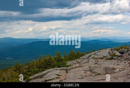 Nordblick vom Mt. Kearsarge Gipfel in Richtung Ragged Mountain. Granitausläufer und gestaute Fichtenbäume. Weit entfernte Gipfel und Grate der White Mountains. Stockfoto