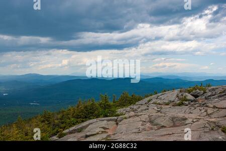 Nordblick vom Mt. Kearsarge Gipfel in Richtung Ragged Mountain. Granitausläufer und gestaute Fichtenbäume. Weit entfernte Gipfel und Grate der White Mountains. Stockfoto