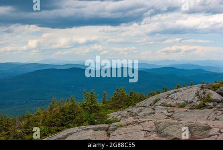 Nordblick vom Mt. Kearsarge Gipfel in Richtung Ragged Mountain. Granitausläufer und gestaute Fichtenbäume. Weit entfernte Gipfel und Grate der White Mountains. Stockfoto