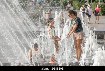 Frau und Mädchen, die sich in Wasserstrahlen abkühlen, gesehen durch Sprays und Tröpfchen, im Sommer, Park von Saint-Petersburg 300 an, Russland Stockfoto