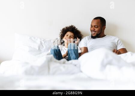 Schwarzer Vater und Sohn lachen, während sie zu Hause im Bett liegen Stockfoto