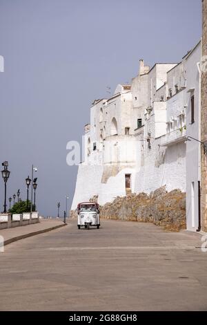 Ostuni ist eine Stadt in der italienischen Region Apulien, die für ihre weiß getünchte Altstadt bekannt ist. Stadtmauer von Ostuni mit Vespa Roller auf der Straße. Süditalien Stockfoto