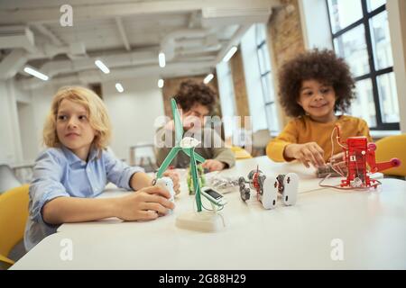 Nahaufnahme von technischen Spielzeugen voller Details auf dem Tisch. Kinder, die am Tisch sitzen und mit Robotern spielen, verbringen Zeit miteinander Stockfoto