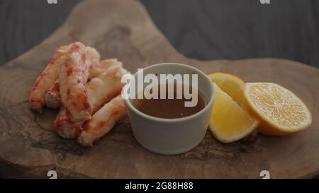 Gimbal-Shot mit Krabbenbein in Zeitlupe auf einem Olivenbrett mit süßer Zitrone und Dip-Sauce, 120 Bilder/s. Stockfoto