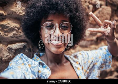Selbstbild einer afrikanisch-fröhlichen Frau. Sie lächelt und tut mit ihren Fingern das Siegeszeichen. Konzept von Glück und Positivität Stockfoto