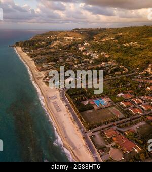 Luftaufnahme eines Sonnenuntergangs über dem Meer in Zambrone, Küste von Kalabrien. Italien. Häuser und Bäume in der Nähe des Strandes mit Sonnenschirmen. Ferienorte, Urlaub Stockfoto