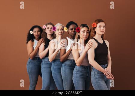 Sechs verschiedene Weibchen stehen zusammen auf braunem Hintergrund. Frauen unterschiedlichen Alters mit Blumen im Haar. Stockfoto