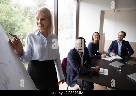 Glücklicher, reifer Business-Lehrer, Coach, der einem vielfältigen Team einen Workshop gibt Stockfoto