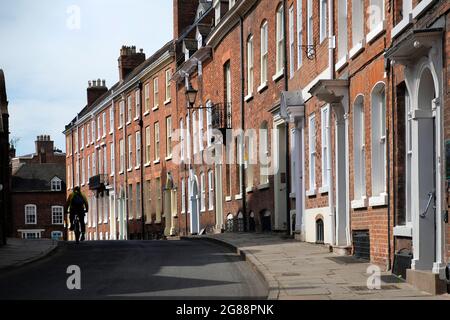 Ein Radler fährt mit seinem Fahrrad auf den St. John's Hill, Shrewsbury, Shropshire, England, Großbritannien. Er ist in Silhouette und fährt an den georgischen Häusern vorbei Stockfoto