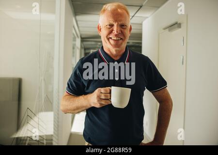 Porträt eines glücklichen Senior Managers, der Kaffee bei der Arbeit trinkt. Geschäftsmann macht Kaffeepause bei der Arbeit. Stockfoto