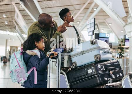 Mann zeigt Tochter und Frau etwas, während er am internationalen Flughafen steht. Dreiköpfige Reisende Familie, die auf den Flug wartet und sich das Timing Eber ansieht Stockfoto