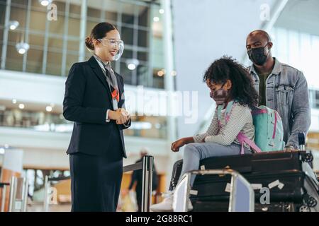 Flughafenmitarbeiter stehen am Flugsteig, das Mädchen sitzt auf dem Gepäck und der Vater schiebt den Trolley. Der Bodenwächter am Flughafen half den Touristen Stockfoto