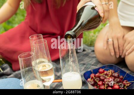 Das Mädchen gießt Wein in ein Glas. Mädchen bei einem Picknick. Eine Frau hält eine Flasche Wein in der Hand. Alkohol trinken in der Natur. Stockfoto