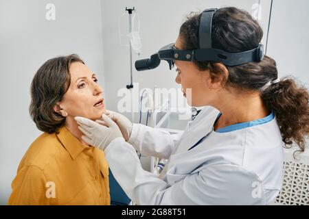 HNO-Arzt, der eine ältere Frau untersucht. Die reife Patientin öffnete ihren Mund zur Kehlkopfprüfung Stockfoto