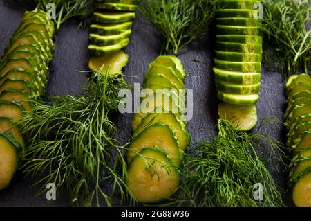 Natürliche, frische grüne Gurken aus einem heimischen Garten auf schwarzem Hintergrund, ein Dummy-Brett aus Stein. Die Gurken werden in Stücke geschnitten und angeordnet Stockfoto