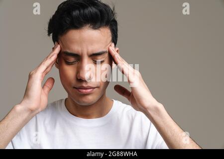 Brünette hispanischen Mann mit Kopfschmerzen reiben seine Schläfen isoliert über grauen Hintergrund Stockfoto