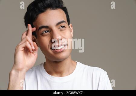 Lächelnder junger Brünette Mann im T-Shirt, der über grauem Wandhintergrund steht Stockfoto