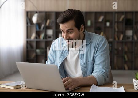 Überraschte junge männliche Arbeiter, die auf den Laptop-Bildschirm schauend. Stockfoto