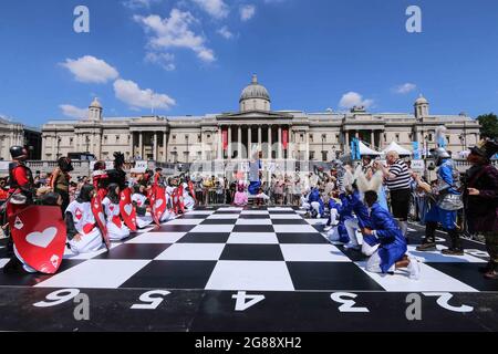 London 18 July 2021 Schachfest auf dem Trafalgar Square, EIN Riesensprung von einem der Schauspieler, die sich entlang des Brettes bewegen, forganisiert von der Wohltätigkeitsorganisation Chess in Schools and Communities, deren Mission es ist, die Bildungsergebnisse und die soziale Entwicklung von Kindern zu verbessern, indem sie sie in das Schachspiel einführen. 32 Schauspieler, die als Alice durch die Looking Glass Charaktere gekleidet waren, spielten ein Spiel basierend auf dem Buch in einem riesigen Schachbrett. Paul Quezada-Neiman/Alamy Live News Stockfoto