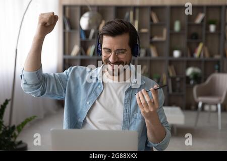 Fröhlicher junger Mann, der energiegeladene Musik aus der mobilen Wiedergabeliste hört. Stockfoto