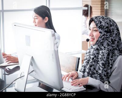 Eine wunderschöne muslimische Servicearbeiterin lächelt selbstbewusst, während sie Kunden am Arbeitsplatz berät und ihnen hilft. Stockfoto