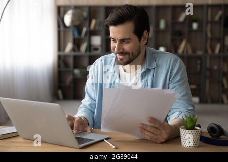 Glücklicher junger Geschäftsmann, der mit Dokumenten am Computer arbeitet. Stockfoto