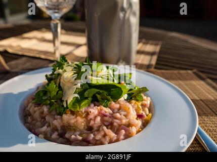 Sommeressen im Freien bei Sonnenschein: Krabbenfleisch- und Zwiebelrisotto mit rasierten Fenchel, Basilikum und Petersilie, Kristallweinglas und Weinkühler Stockfoto