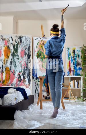Die ganze Länge der Künstlerin hob ihre Hand mit Pinsel in ihm, während sie an ein neues Gemälde denken, die Schaffung zu Hause Studio-Workshop Stockfoto