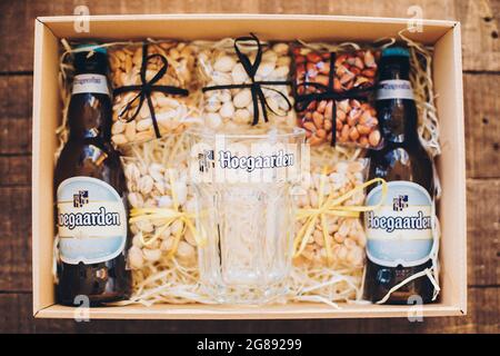 Lviv, Ukraine - 1. Dezember 2017: Hoegaarden Bierflasche und Glasbecher mit Etikett und gesalzene Nüsse Snacks auf Stroh in Geschenkbox. Stilvolle Geschenkbox für ma Stockfoto