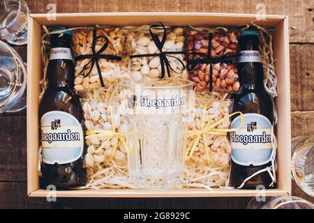 Lviv, Ukraine - 1. Dezember 2017: Hoegaarden Bierflasche und Glasbecher mit Etikett und gesalzene Nüsse Snacks auf Stroh in Geschenkbox. Stilvolle Geschenkbox für ma Stockfoto