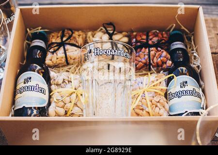 Lviv, Ukraine - 1. Dezember 2017: Hoegaarden Bierflasche, Glasbecher und gesalzene Nüsse Snacks auf Stroh in Geschenkbox. Stilvolle Geschenkbox für Mann Geburtstag, fa Stockfoto