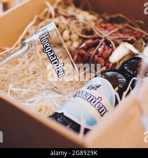 Lviv, Ukraine - 1. Dezember 2017: Hoegaarden Bierflasche, Glasbecher und gesalzene Nüsse Snacks auf Stroh in Geschenkbox. Stilvolle Geschenkbox für Mann Geburtstag, fa Stockfoto