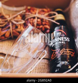 Lviv, Ukraine - 1. Dezember 2017: Guinness Bierflasche, Glasbecher und gesalzene Nüsse Snacks auf Sackleinen in Geschenkbox. Stilvolle Geschenkbox für Mann Geburtstag, Fett Stockfoto