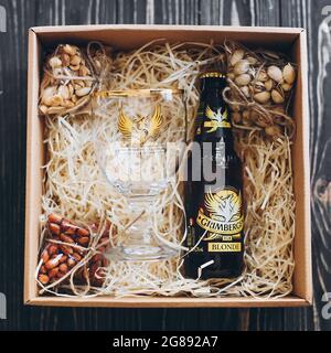 Lviv, Ukraine - 1. Dezember 2017: Grimbergen Bierflasche und Glasbecher mit Etikett und gesalzenen Nüssen Snacks auf Stroh in Geschenkbox. Stilvolle Geschenkbox für ma Stockfoto
