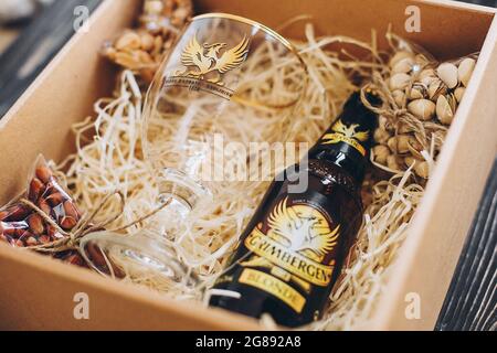 Lviv, Ukraine - 1. Dezember 2017: Grimbergen Bierflasche, Glasbecher und gesalzene Nüsse Snacks auf Stroh in Geschenkbox. Stilvolle Geschenkbox für Mann Geburtstag, fa Stockfoto