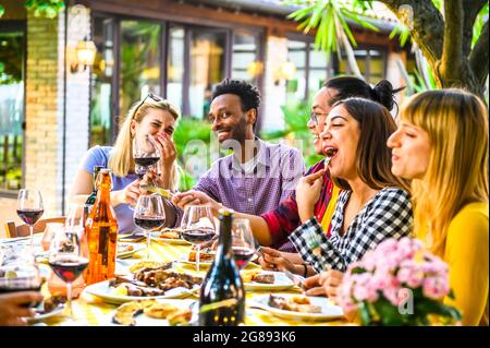 Eine Gruppe von glücklichen multirassischen Freunden, die im Restaurantgarten zu Abend essen - Freundschaftskonzept mit glücklichen Menschen, die gemeinsam Getränke toasten Stockfoto