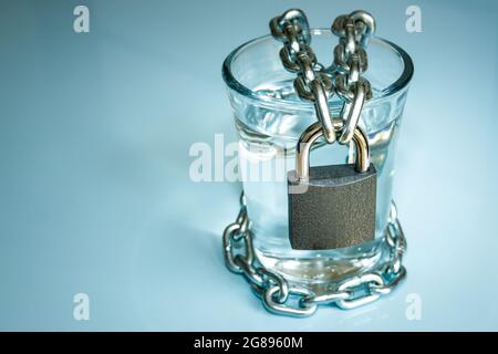 Ein Glas Wasser in einer Kette verpackt und mit einem Vorhängeschloss verschlossen. Das Problem der kleinen Trinkwasserressourcen in der Welt. Umweltschutz CO Stockfoto