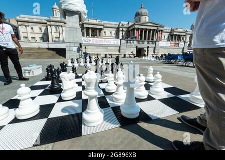 London, Großbritannien. 18. Juli 2021. Ein Freiluftschachspiel im Gange beim Chess Fest auf dem Trafalgar Square. Die Veranstaltung feiert das Schachspiel und Besucher können das Spiel lernen, Schach spielen oder einen Großmeister herausfordern. Anlässlich des 150-jährigen Jubiläums von Lewis Carrolls Buch „Alice durch das schauende Glas“, in dem das Schachspiel vorgestellt wurde, stehen 32 Schauspieler, die als Alice durch die schauenden Glasfiguren gekleidet sind, auf einem riesigen Schachbrett, das ein Spiel basierend auf dem Buch nachspielt. Kredit: Stephen Chung / Alamy Live Nachrichten Stockfoto