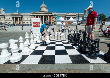 London, Großbritannien. 18. Juli 2021. Ein Freiluftschachspiel im Gange beim Chess Fest auf dem Trafalgar Square. Die Veranstaltung feiert das Schachspiel und Besucher können das Spiel lernen, Schach spielen oder einen Großmeister herausfordern. Anlässlich des 150-jährigen Jubiläums von Lewis Carrolls Buch „Alice durch das schauende Glas“, in dem das Schachspiel vorgestellt wurde, stehen 32 Schauspieler, die als Alice durch die schauenden Glasfiguren gekleidet sind, auf einem riesigen Schachbrett, das ein Spiel basierend auf dem Buch nachspielt. Kredit: Stephen Chung / Alamy Live Nachrichten Stockfoto