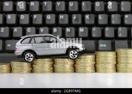 Ein Auto auf einer aufsteigenden Münzsäule mit einer Tastatur im Hintergrund. Eine Metapher für Online-Autokauf, Steuern, Versicherungen und Shopping. Stockfoto