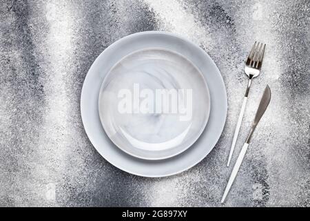 Zwei leere Keramikplatten und sauberes Messer mit Gabel, Geschirr auf einem grauen Grunge-Tisch, Servierkonzept. Flaches Lay-Design. Speisekarte im Restaurant. Grußkarte Stockfoto