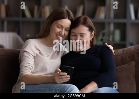 Glückliche reife Mutter und Erwachsene Tochter mit Mobiltelefon zusammen Stockfoto