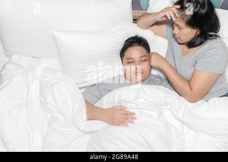 Mutter misst die Temperatur seines kranken Kindes. Krankes Kind mit hohem Fieber liegt im Bett und Mutter fühlt sich gestresst, Gesundheitskonzept. Stockfoto