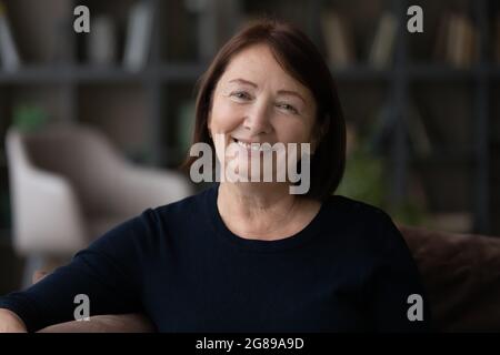 Glückliche ältere Frau, die zu Hause auf der Couch sitzt Stockfoto