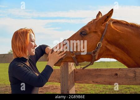 An einem sonnigen Sommertag streichelte ein rothaariges Mädchen im Fahrerlager Stockfoto