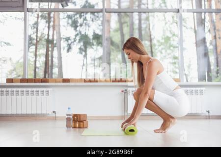 Eine Barfußfrau dreht eine lila Yogamatte und Fitness auf dem Parkettboden. Stockfoto