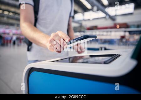 Hand eines Mannes während der Nutzung des Check-in-Automaten. Passagier scannt Ticket auf Smartphone am Flughafenterminal. Stockfoto